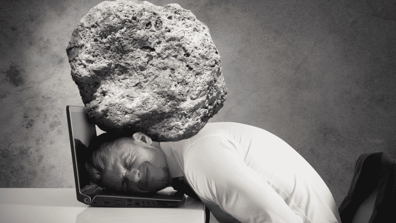 Homem na frente do notebook com uma pedra pesando em seus ombros