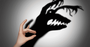 Mão fazendo sombra em uma parede. A sombra está aparecendo diferente, na forma de um monstro