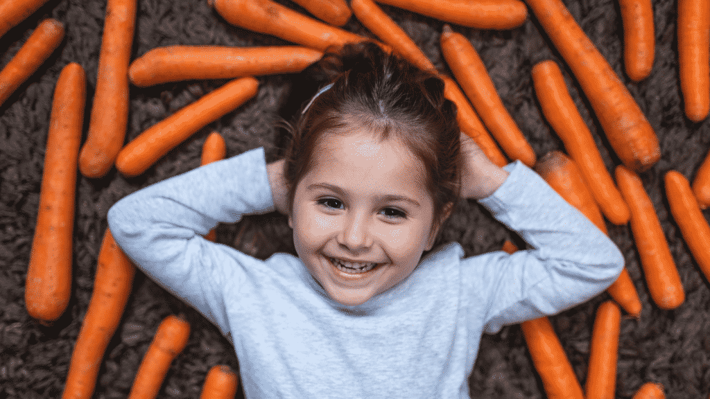 Uma criança deitada num chão repleto de cenouras.