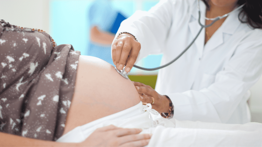 Um profissional da saúde, com um estetoscópio, examinando a barriga de uma mulher grávida