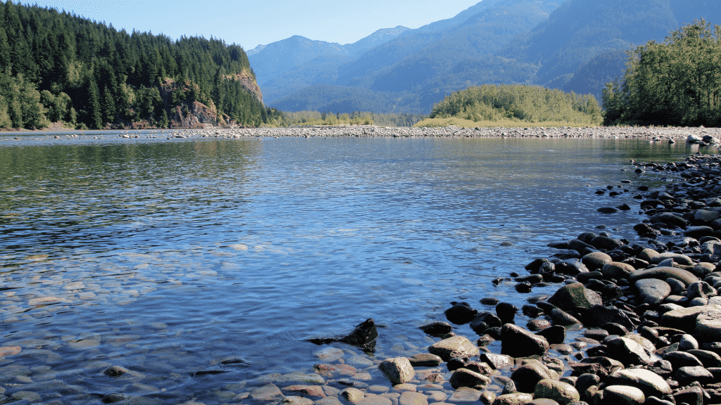 Um rio com água limpa. Ao fundo, montanhas.