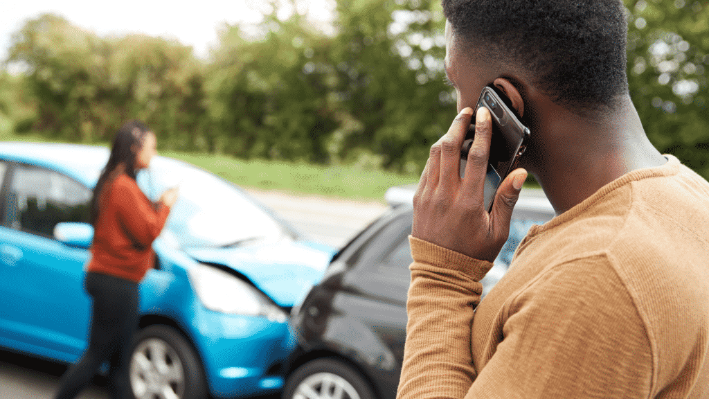 Um homem observando um acidente de carro e realizando uma ligação via telefone celular.
