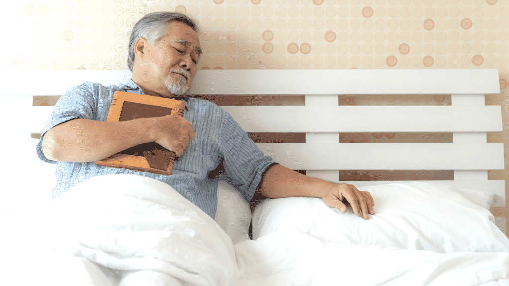 Um homem deitado numa cama, segurando um quadro e olhando o lado esquerdo de sua cama.