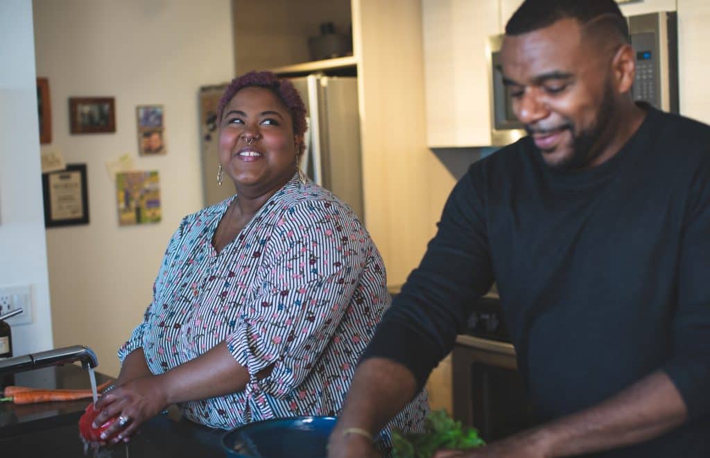 Mulher e homem negros lavando legumes.