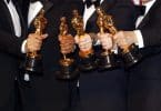 Estatuetas do Oscar sendo seguradas por pessoas.