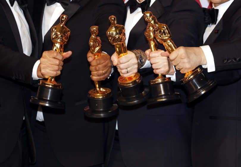 Estatuetas do Oscar sendo seguradas por pessoas.
