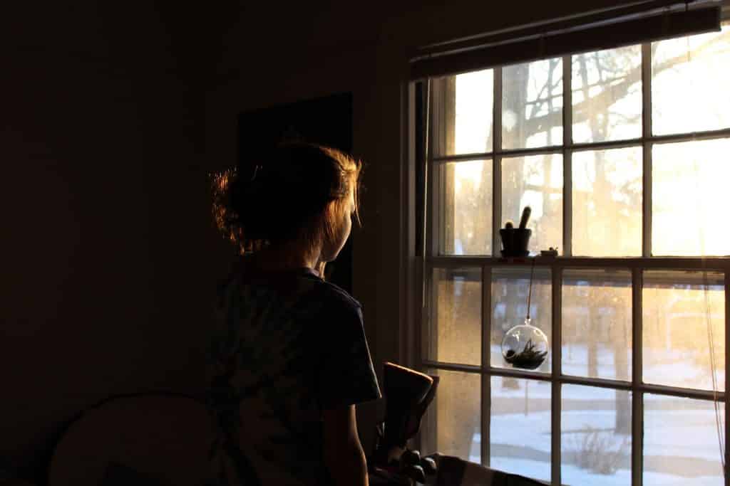Menina de costas olhando por uma janela.