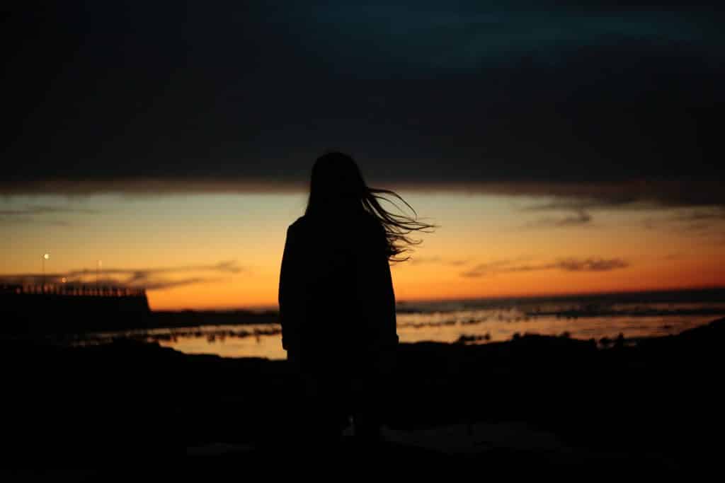 Silhueta de uma mulher olhando o mar ao anoitecer.