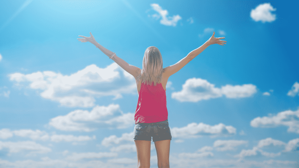 Uma mulher de braços erguidos em frente a um céu azul.