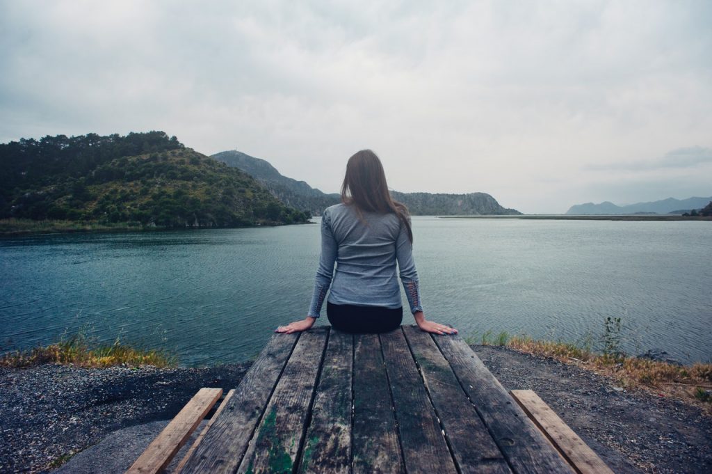 Mulher sentada em uma ponte olhando para o horizonte em um lago.