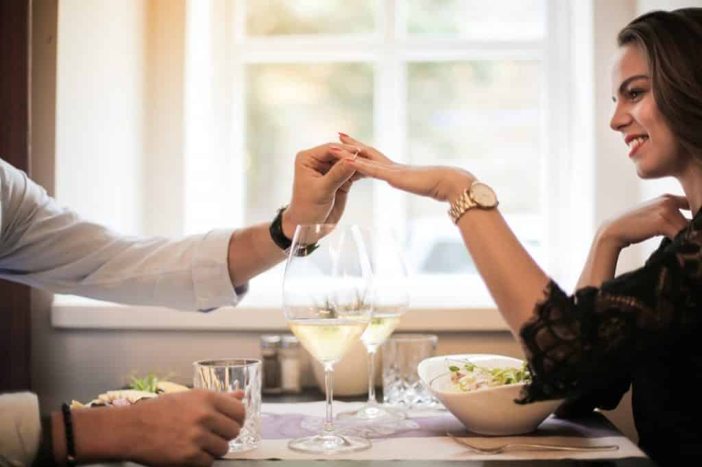 Homem em um jantar romântico colocando um anel no dedo da mulher.