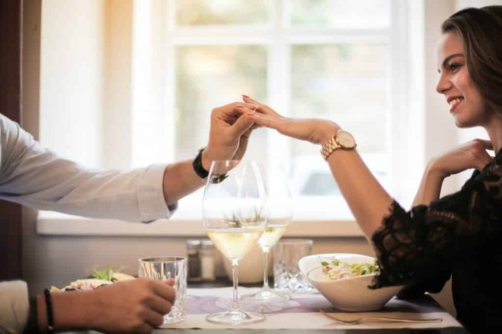 Homem em um jantar romântico colocando um anel no dedo da mulher.