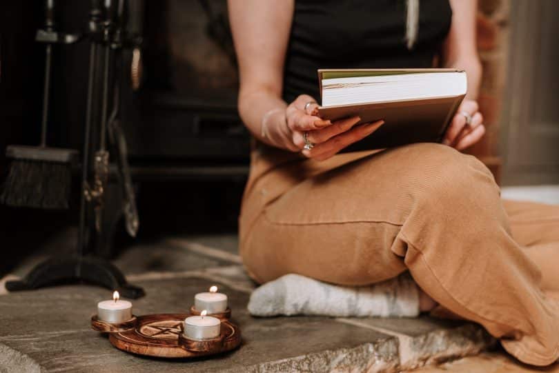 Mulher segurando livro com velas ao seu lado