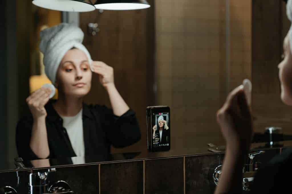 Mulher fazendo skin care na frente do espelho com o celular gravando em formato de live.
