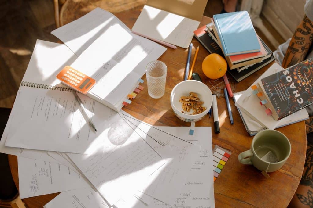 Mesa com papéis, canetas, canecas e livros bagunçados.