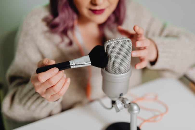 Mulher com um microne e um pincel para praticar asmr