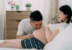 Uma mulher grávida e, ao seu lado, um homem beijando sua barriga.
