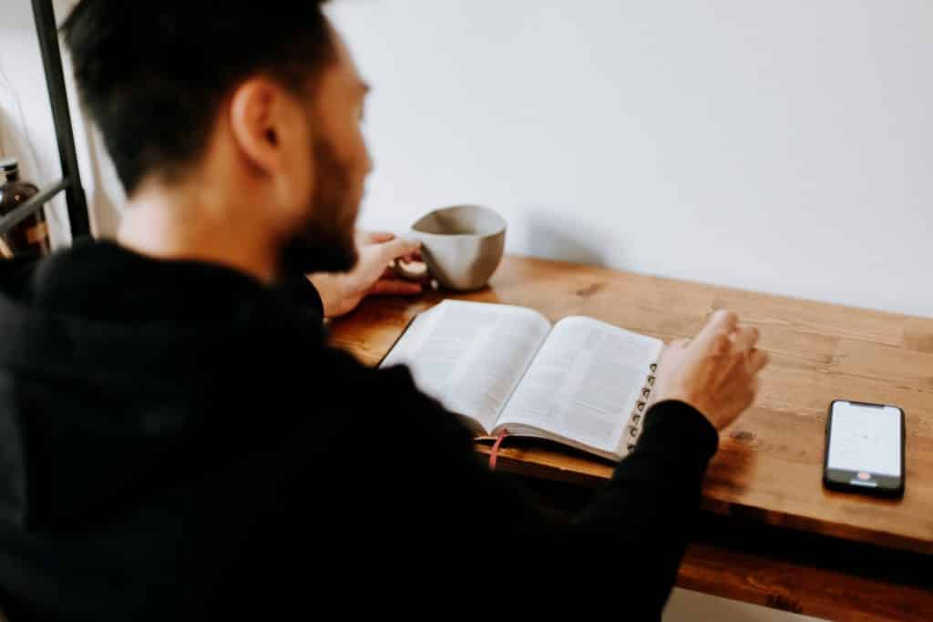 Homem branco lendo livro na mesa.