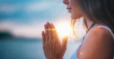 Mulher com os olhos fechados e as mãos juntas em forma de oração.