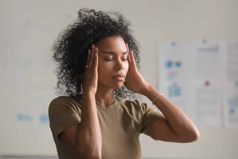 Mulher negra com os olhos fechados e com as mãos em suas têmporas