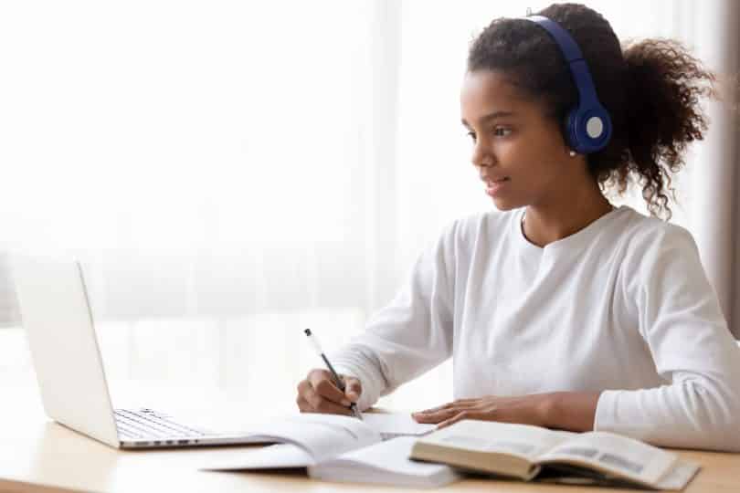 Menina sentada em frente a um computador estudando.