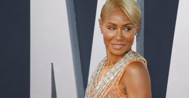 Jada Smith com o cabelo loiro, roupa de brilho e dourada, olhando para o lado