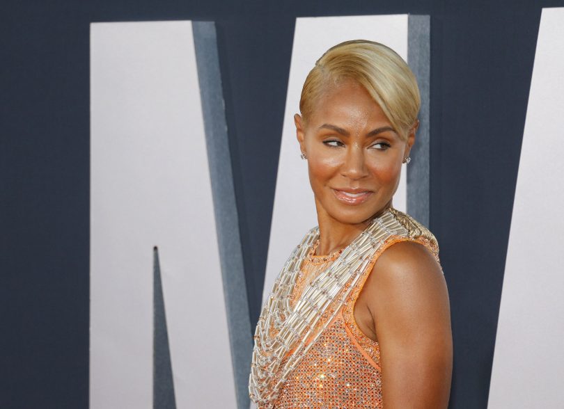 Jada Smith com o cabelo loiro, roupa de brilho e dourada, olhando para o lado