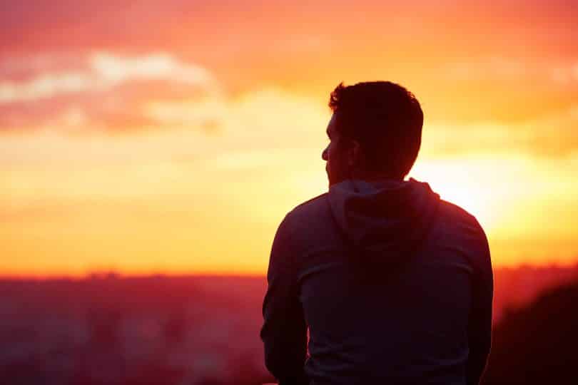 Homem sentado de costas olhando o por do sol.