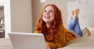 Mulher ruiva deitada na cama olhando para cima e sorrindo.