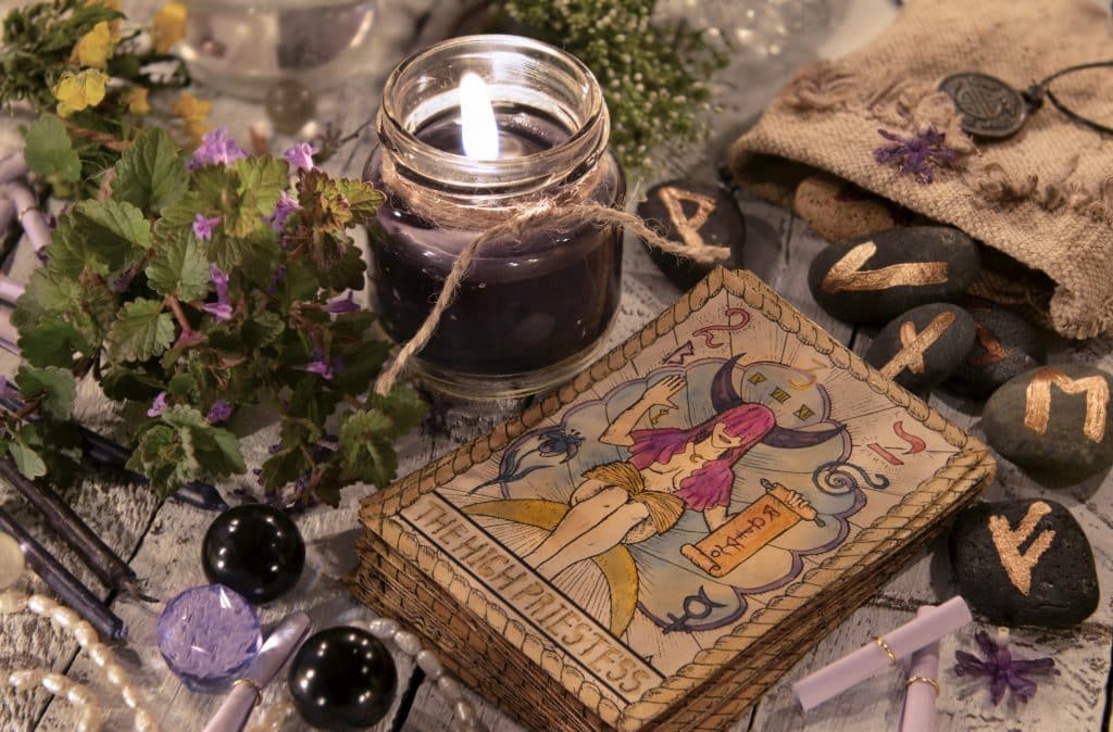Cartas de tarot em uma mesa com pedras de runa, plantas e uma vela.