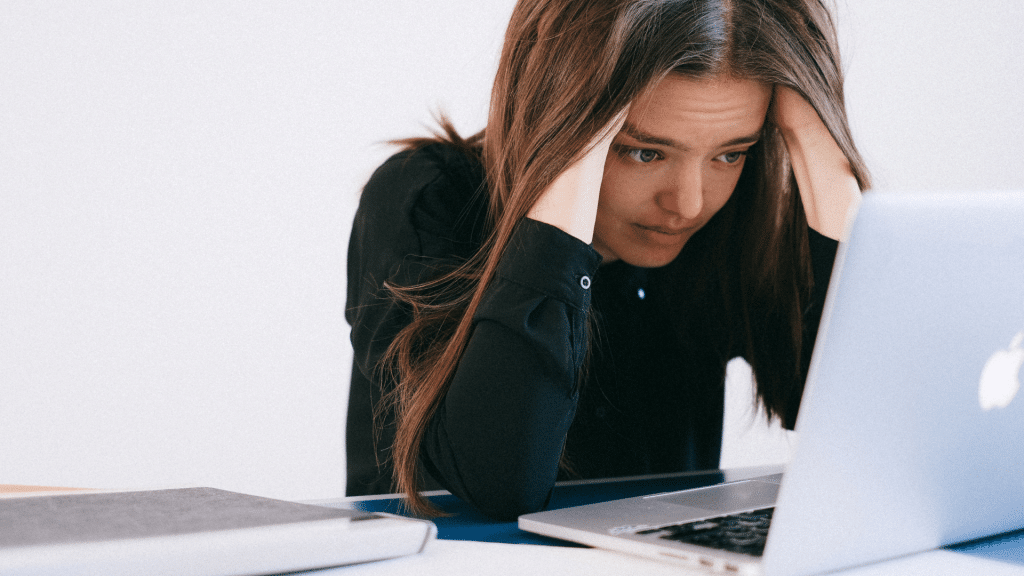 Mulher branca com as mãos na cabeça olhando angustiada para o computador