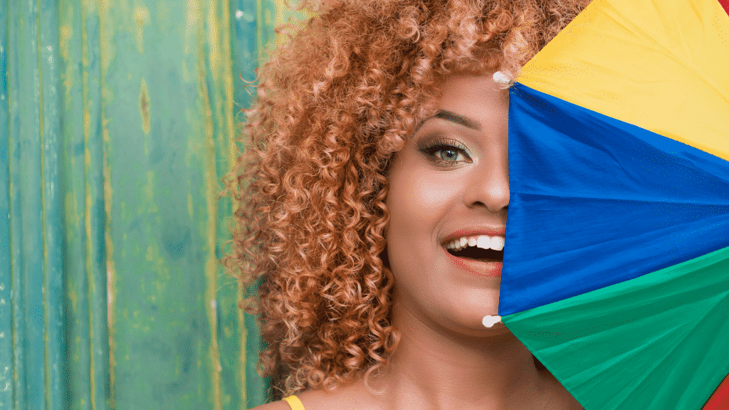 Mulher sorrindo com um mini guarda chuva colorido cobrindo metade do seu rosto