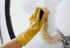 Pessoa vestindo luvas limpando um espelho com esponja e sabão