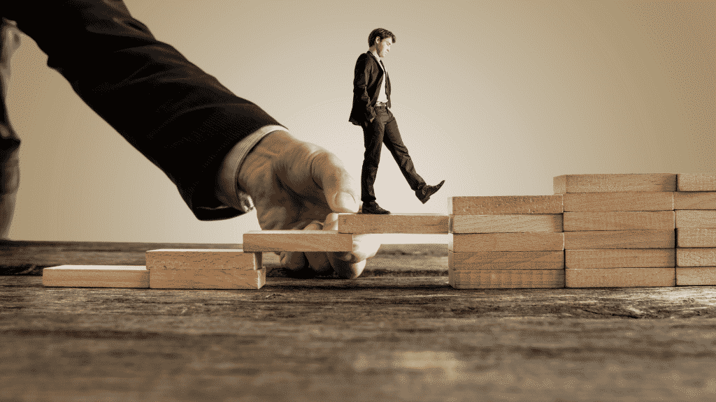 Ilustração de um homem pequeno dando passos em uma escadinha feita de blocos de madeira. Ao fundo, uma pessoa está montando a escada