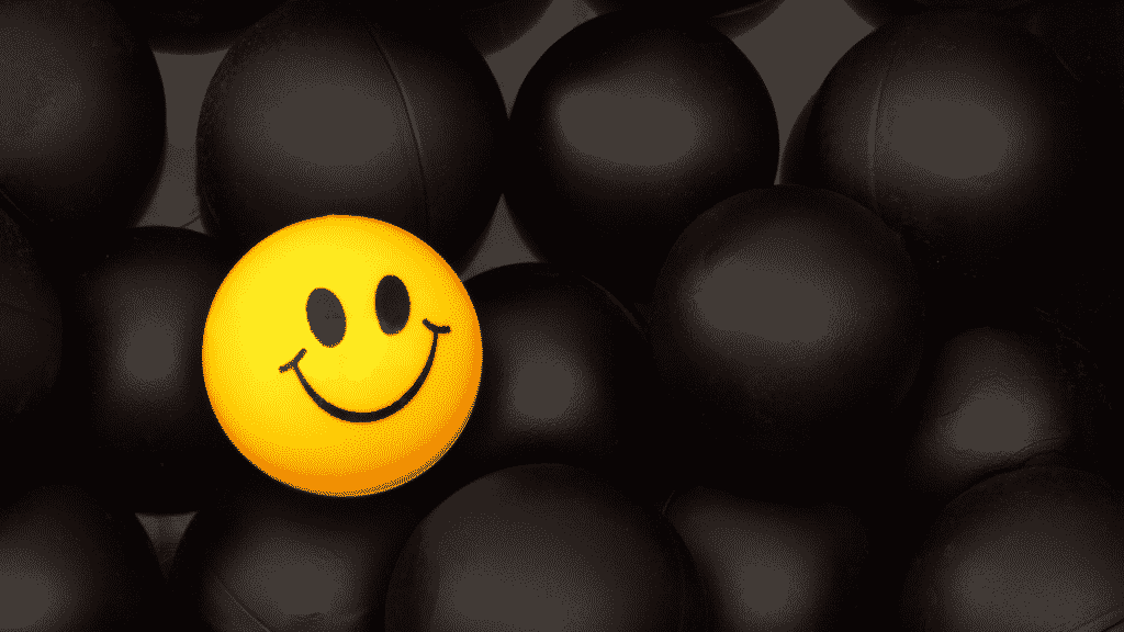 Bola amarela com sorriso desenhado entre diversas bolas pretas