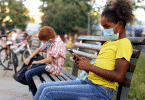 Crianças com máscaras sentadas em um banco, mantendo o distanciamento social