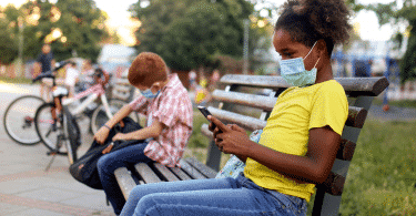 Crianças com máscaras sentadas em um banco, mantendo o distanciamento social