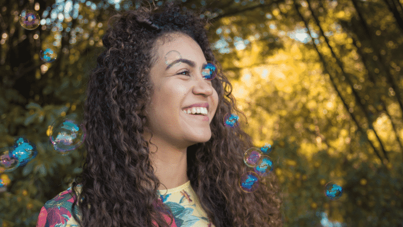 Mulher sorrindo com bolhas de sabão flutuando em um parque