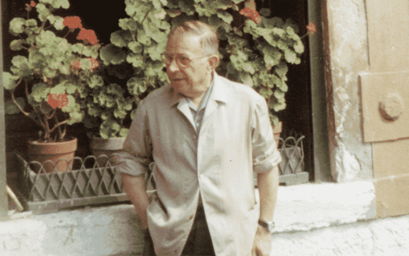 O filósofo Jean Paul Sartre próximo à uma janela repleta de vasos de rosas.