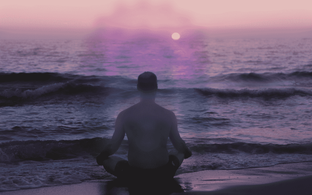 Uma pessoa sentada às margens de um grande curso de água. Dela, emite-se uma aura colorida.