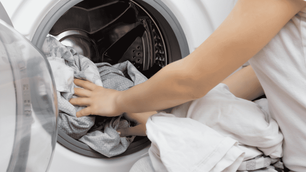 Uma pessoa colocando roupas sujas numa máquina de lavar roupas.