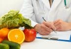 À esquerda, frutas e verduras. À direita, um médico de jaleco escrevendo alguma coisa em seu caderno.