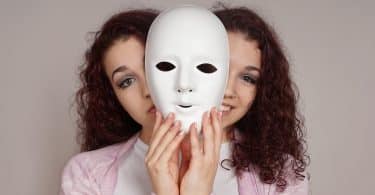 Uma mulher de duas cabeças, apresentando diferentes expressões. Entre elas, duas mãos que seguram uma máscara.