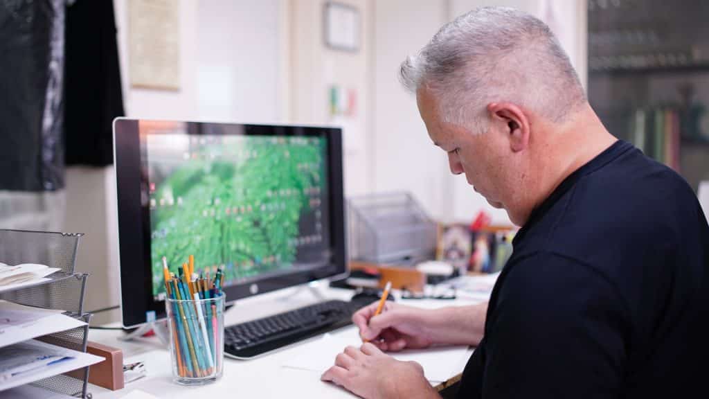 Homem sentado em uma mesa de escritório escrevendo algo em um papel.