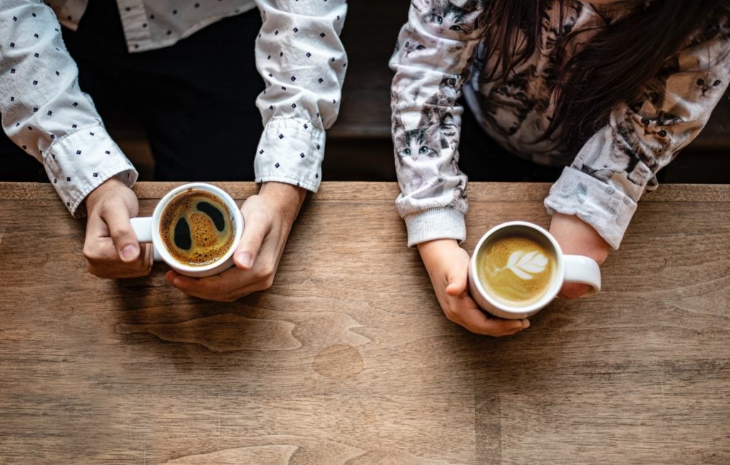 Duas pessoas sentadas lado a lado tomando café.