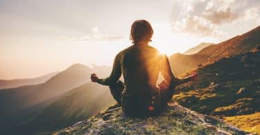 Um homem meditando no pico de um cume.