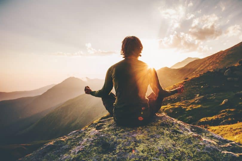 Um homem meditando no pico de um cume.