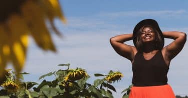 Mulher negra de olhos fechados e sorrindo num campo.