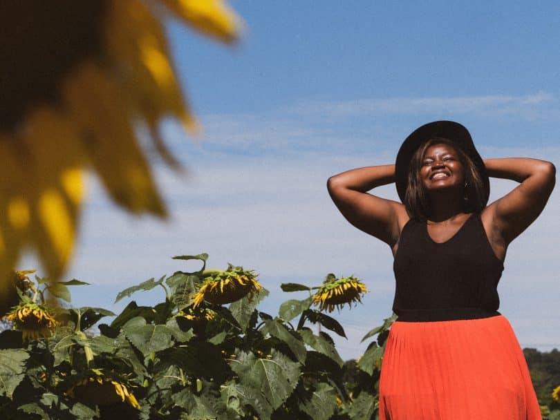 Mulher negra de olhos fechados e sorrindo num campo.