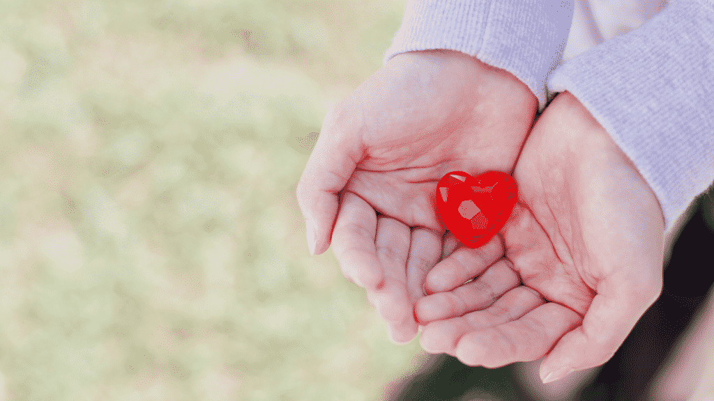 Mãos segurando um cristal em formato de um coração vermelho.